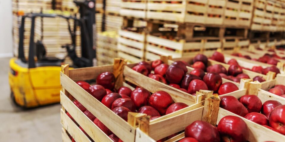 Stacks of crated red apples waiting to be loaded onto trailers for final delivery. A forklift is in the background.