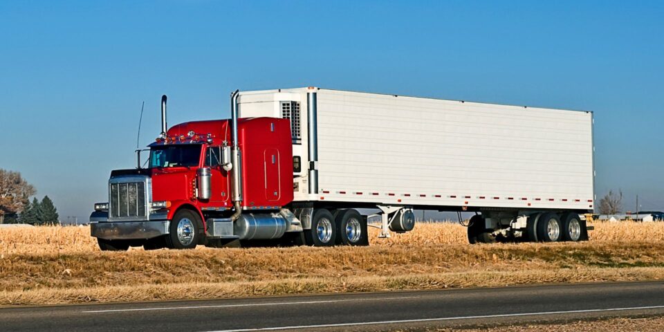 A red semi truck and refrigerated trailer traveling a sunny highway