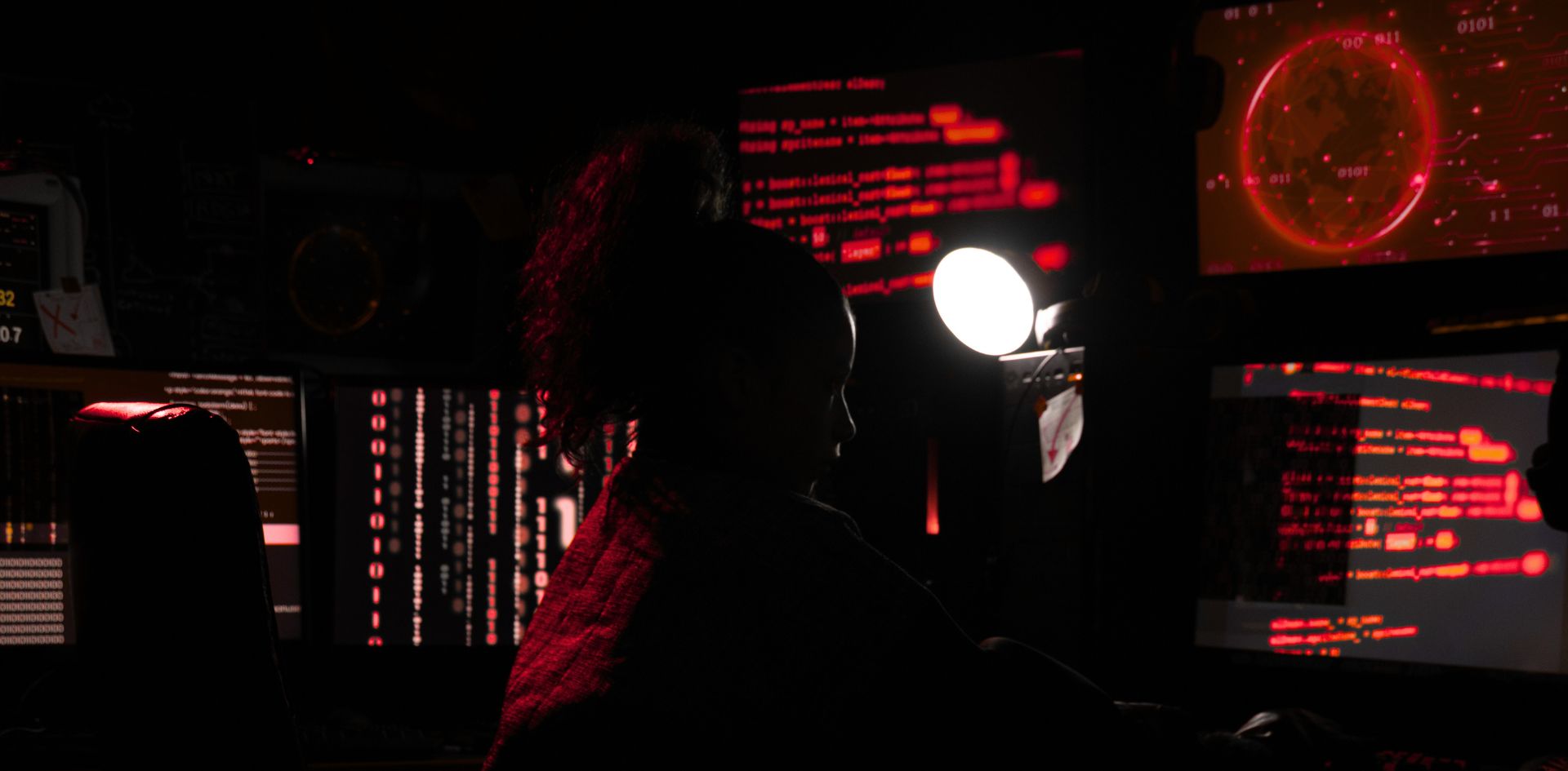 A silhouetted women working at a set of computer screens. She's engaged in freight fraud, empowered by generative AI tools.