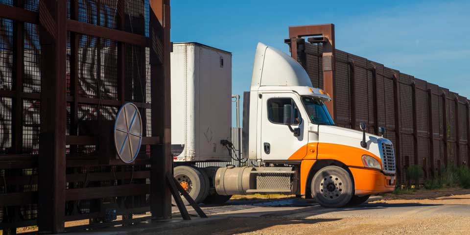 A white and orange semi truck crossing the United States - Mexico border